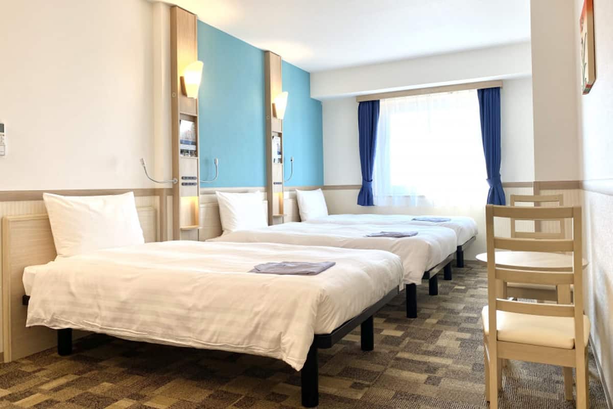 Une chambre d’hôtel avec deux lits, une chaise et une fenêtre avec des rideaux.