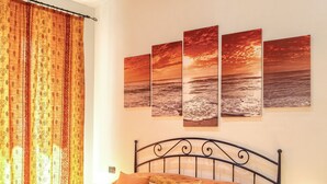 A bedroom with a large bed, a nightstand, and three sunset paintings on the wall.