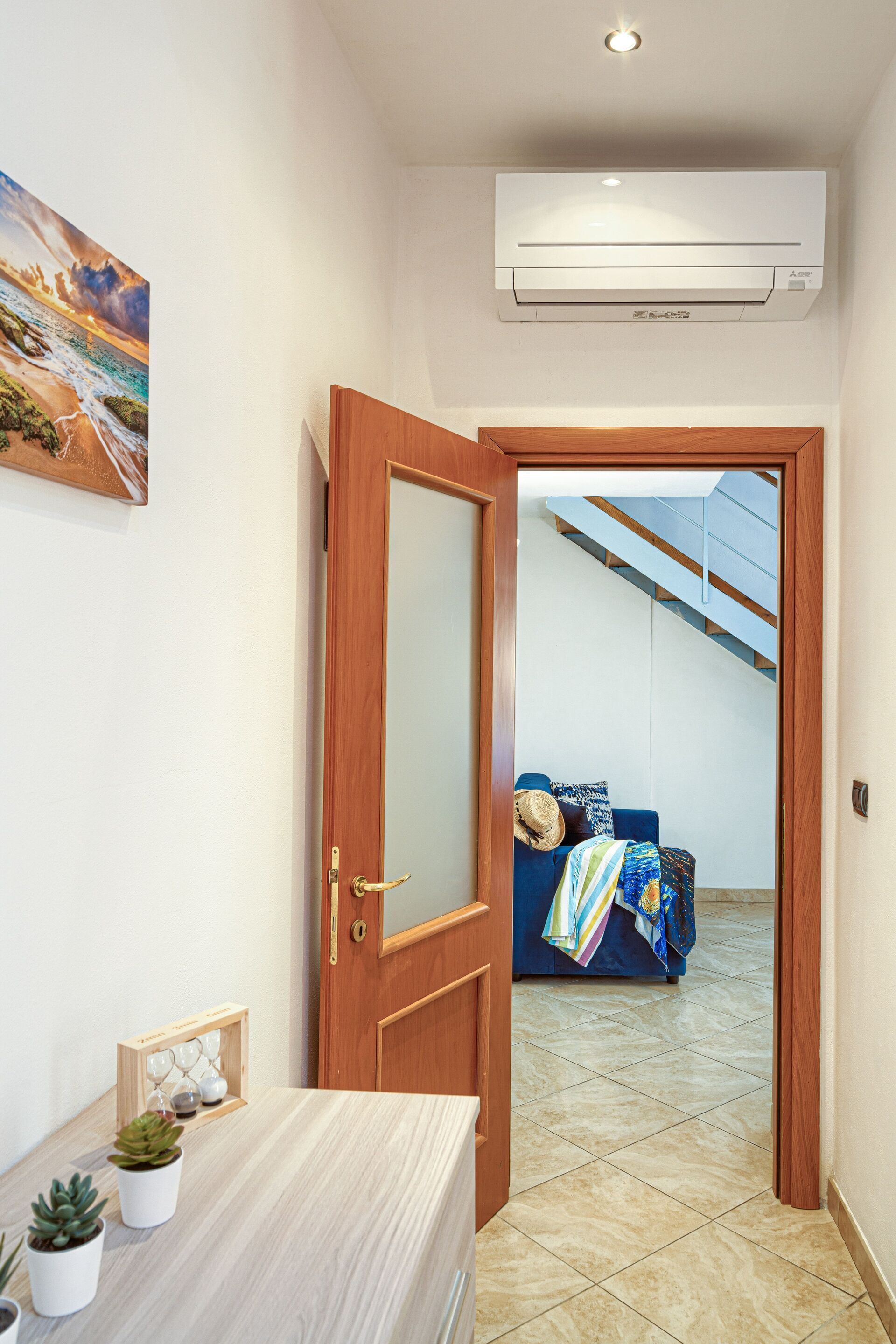 Un corridoio con una porta in legno che dà su una stanza con un divano blu e un quadro raffigurante una spiaggia.