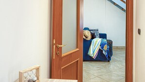A hallway with a wooden door leading to a room with a blue sofa and a beach painting on the wall.