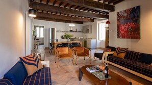 A spacious living area with a sofa, chairs, and a coffee table. There is a kitchen in the background with modern appliances.