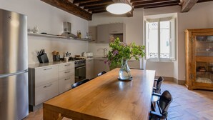 A kitchen with a wooden table, chairs, a refrigerator, and a vase with flowers.