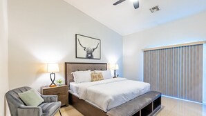 Quarto moderno com uma cama grande, mesas de cabeceira, uma cadeira e um ventilador de teto.