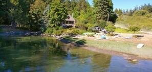 Un chalet au bord du lac, doté d’un quai, entouré d’une forêt dense et surplombant un ciel dégagé.