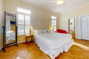 A spacious bedroom with a large bed, two bedside lamps, a mirror, and a red chair.