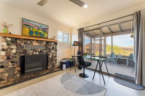 Una sala de estar con chimenea de piedra, un cuadro, una zona de comedor con mesa de vidrio y vistas al exterior.