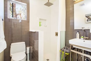 A bathroom with a toilet, shower, sink, and a window with a view of trees.