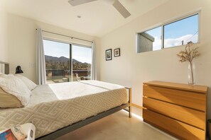 A bedroom with a bed, a dresser, a window with a view of the outdoors, and a ceiling fan.