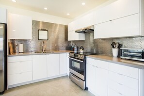 Una cocina moderna con armarios blancos, un refrigerador de acero inoxidable, horno integrado y salpicadero de azulejos.