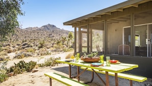 Un paysage désertique avec une table et des bancs en bois, un pot de cactus et une vue sur les montagnes.
