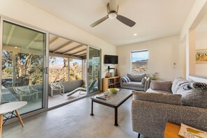 A modern living room with a glass sliding door leading to a patio, a ceiling fan, a flat-screen TV, and a comfortable seating area. - Joshua Tree Dream Weaver a chic home on 5 private acres (Joshua Tree)