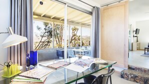 Une chambre moderne avec une table en verre, une lampe et une vue sur les arbres à l’extérieur.