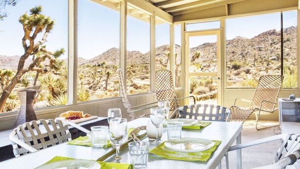 Un coin repas avec une table dressée pour deux personnes, donnant sur un paysage désertique parsemé de cactus et dominé par des montagnes.