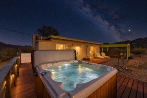 A hot tub on a wooden deck with a house in the background, under a starry night sky.