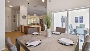 A dining area with a wooden table set for four, a vase with plants, and a view into the kitchen and dining room.