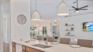A modern kitchen with a large island, pendant lights, and a ceiling fan.