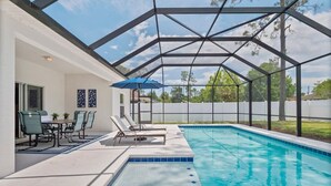 A swimming pool with a covered patio area, including lounge chairs and a table.