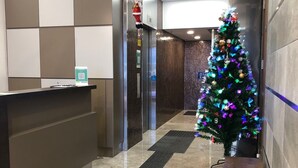 A hotel lobby with a reception desk, a Christmas tree, a bench, and a tiled floor. - WE Hotel Kowloon (Kowloon)