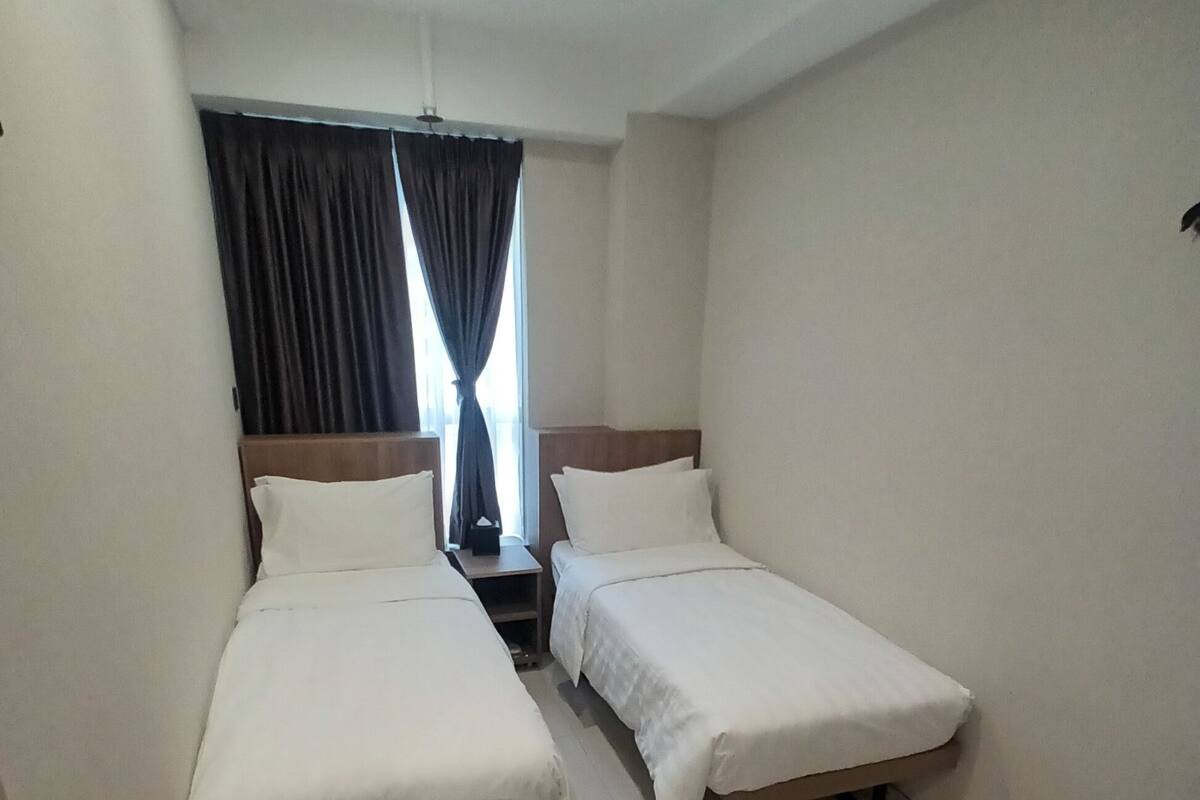 A hotel room with two single beds, a small table, and a window with curtains.