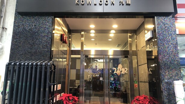 The entrance of a hotel with a modern design, featuring glass doors and a signboard with the hotel's name. - WE Hotel Kowloon (Kowloon)