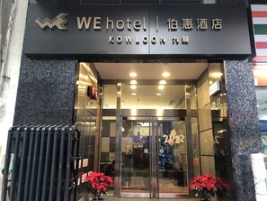 The entrance of a hotel with a modern design, featuring glass doors and a signboard with the hotel's name. - WE Hotel Kowloon (Kowloon)