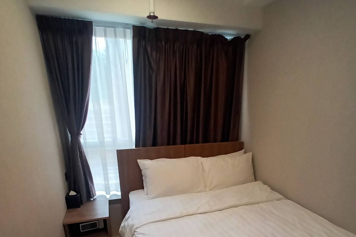A bedroom with a bed, a nightstand, a ceiling fan, and a window with curtains.
