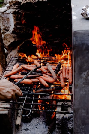 En grill med pølser og gulerødder, der tilberedes over åben ild.