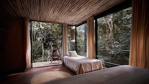 A bedroom with a large bed, a wooden floor, and a view of trees through large windows.