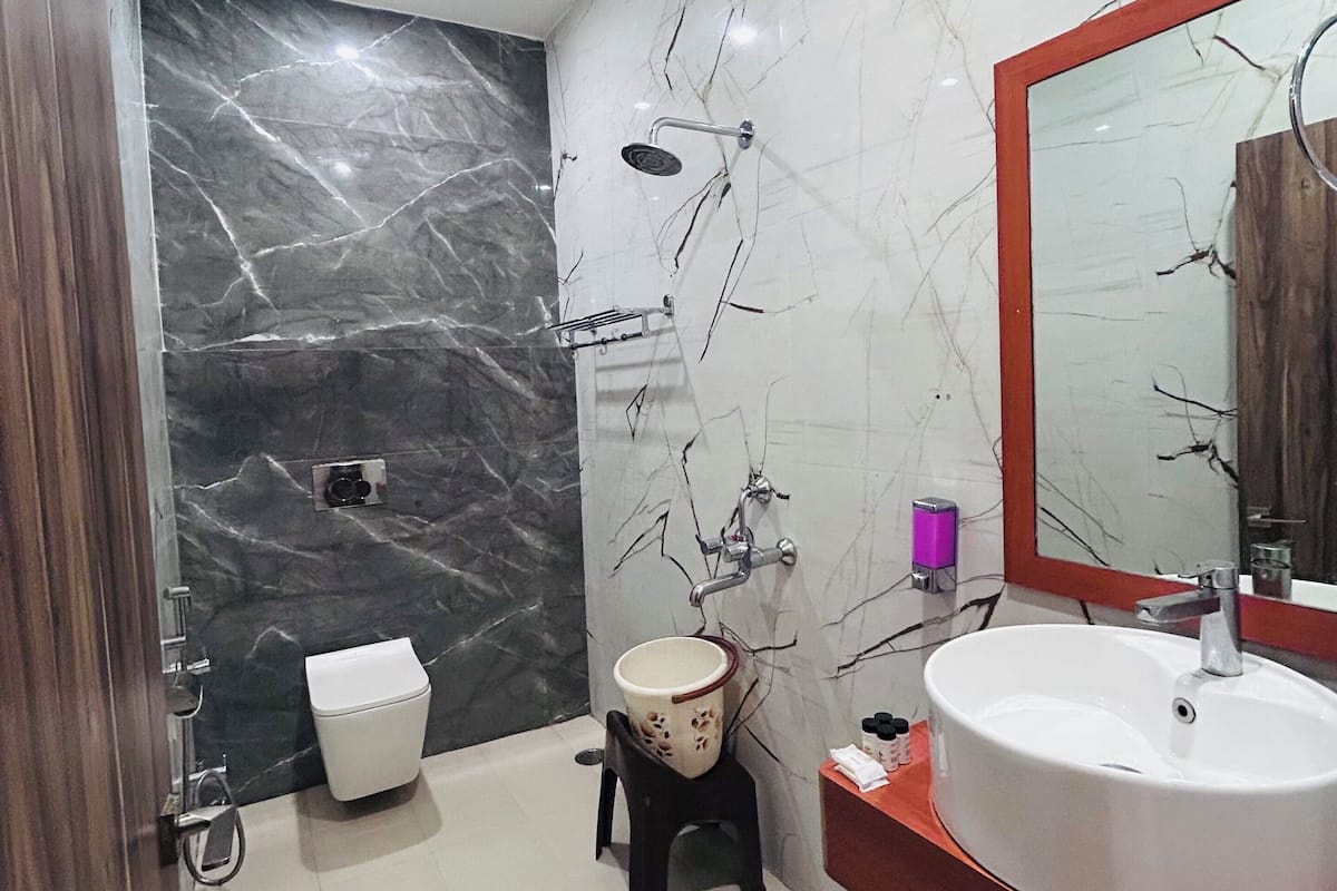 A bathroom with a marble wall, a sink, a toilet, and a shower.
