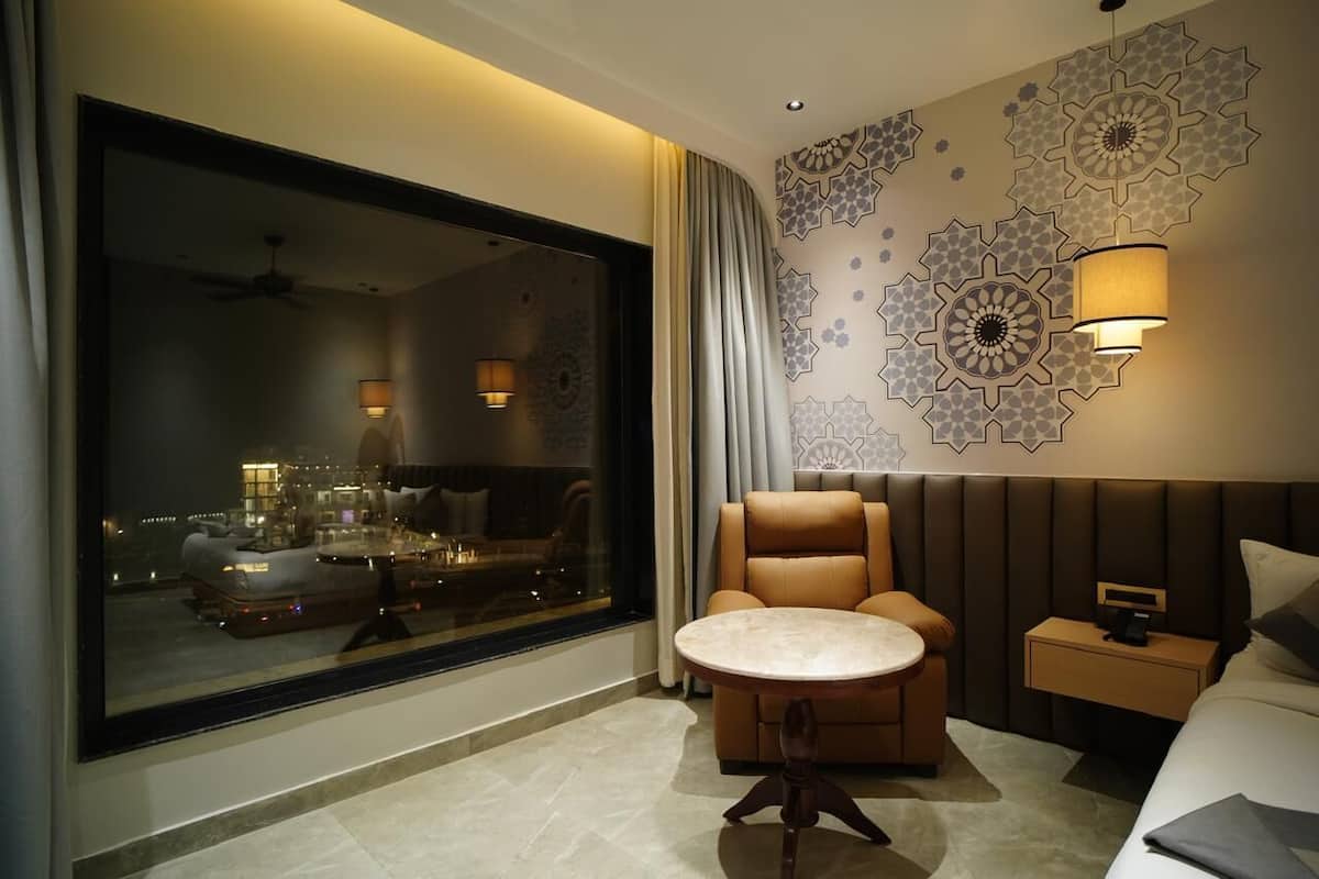 A modern hotel room with a large window, a sofa, a round table, a bed, and decorative wall art.