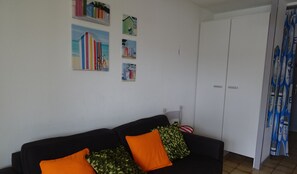 Una sala de estar con un sofá negro, cojines naranja y verde, y una puerta con cortina.
