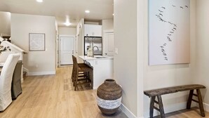 A modern kitchen with white cabinets, a central island, and a dining area with a bench and chairs. - Magnolia Lane by RedAwning (Washington)