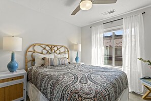 Ein Schlafzimmer mit einem Bett, zwei Nachttischen, einem Deckenventilator und einem Fenster mit Vorhängen.