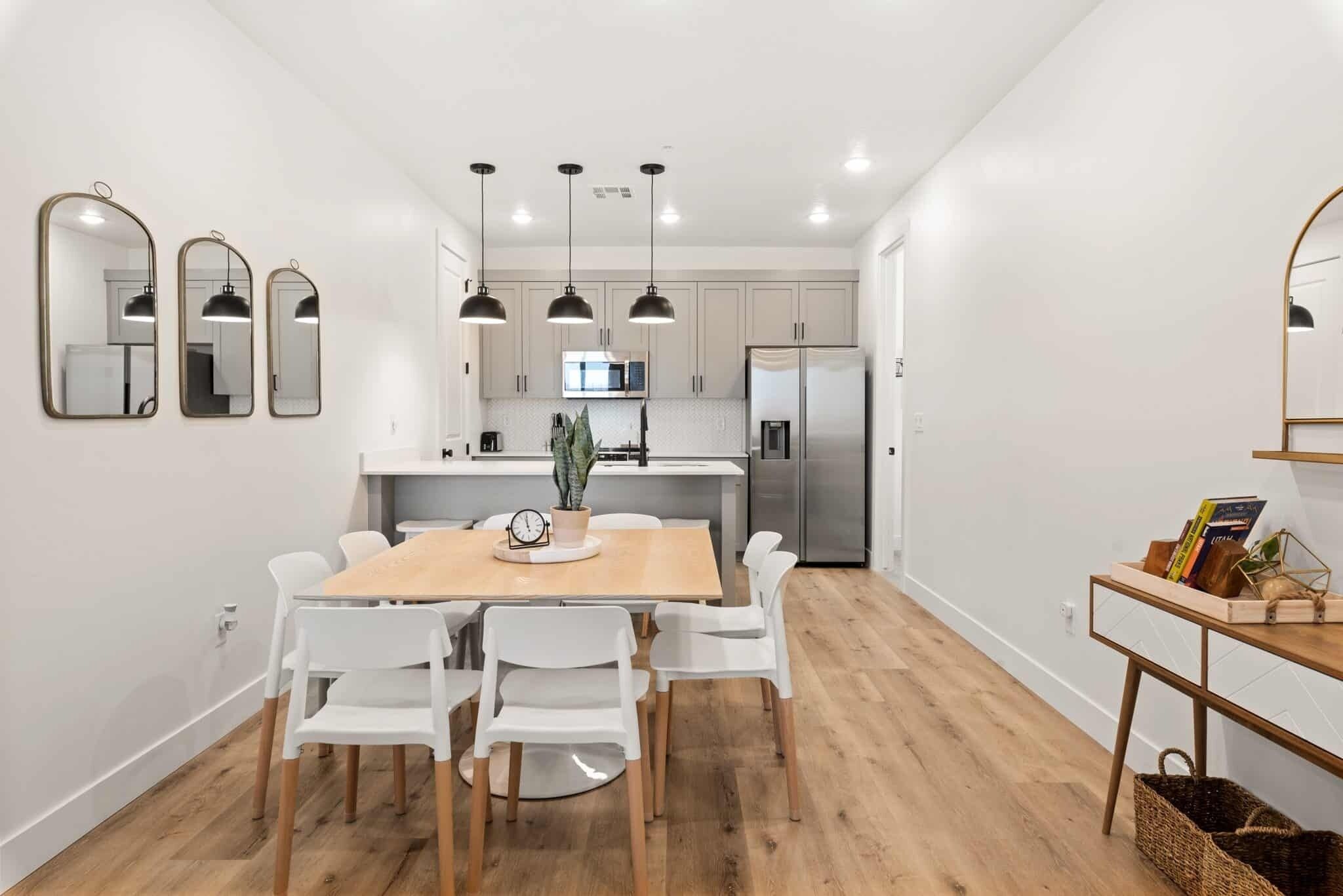Een moderne keuken met witte kastjes, een houten eettafel en hanglampen.