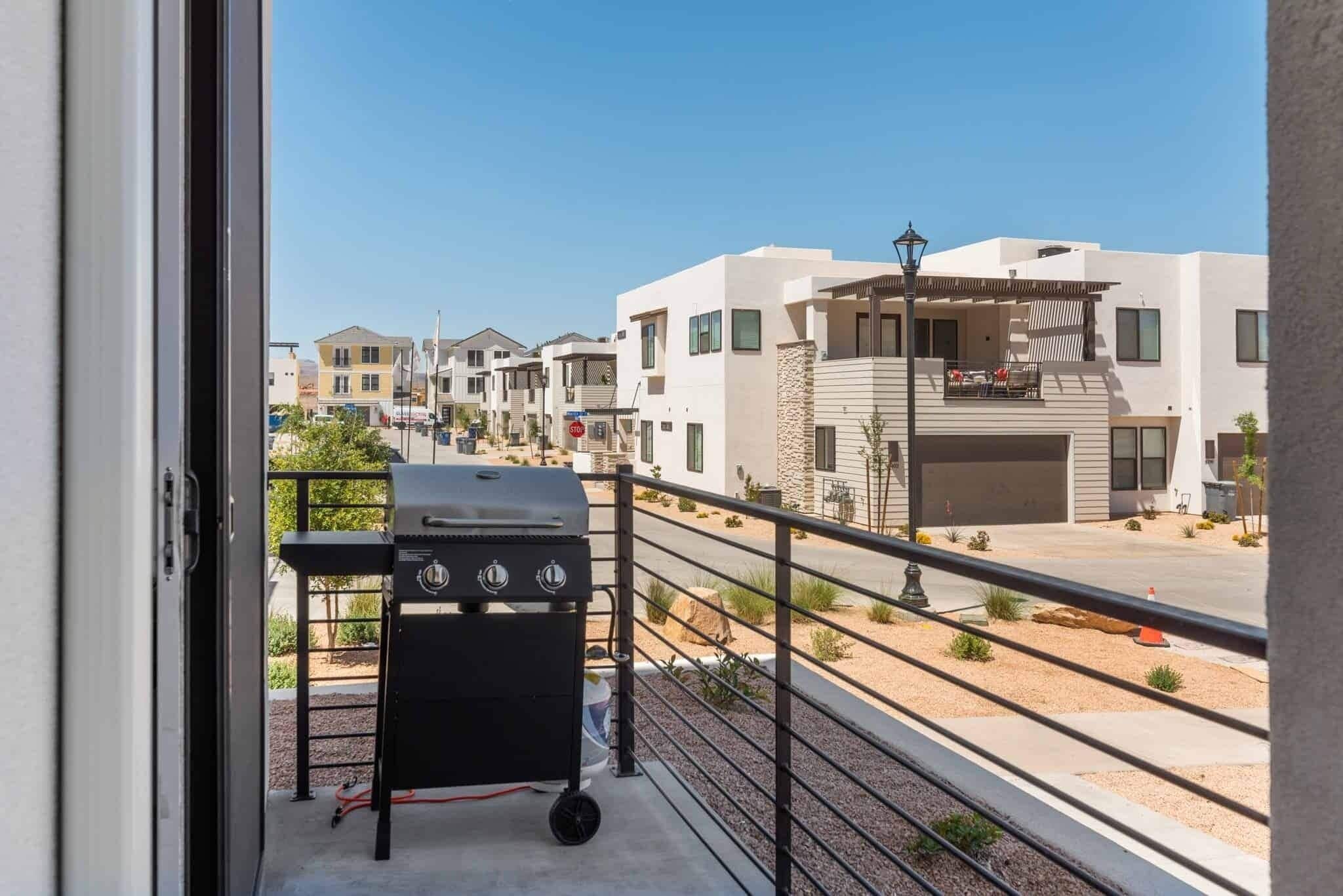 Un balcon avec un barbecue, une vue sur des immeubles modernes et un ciel dégagé.
