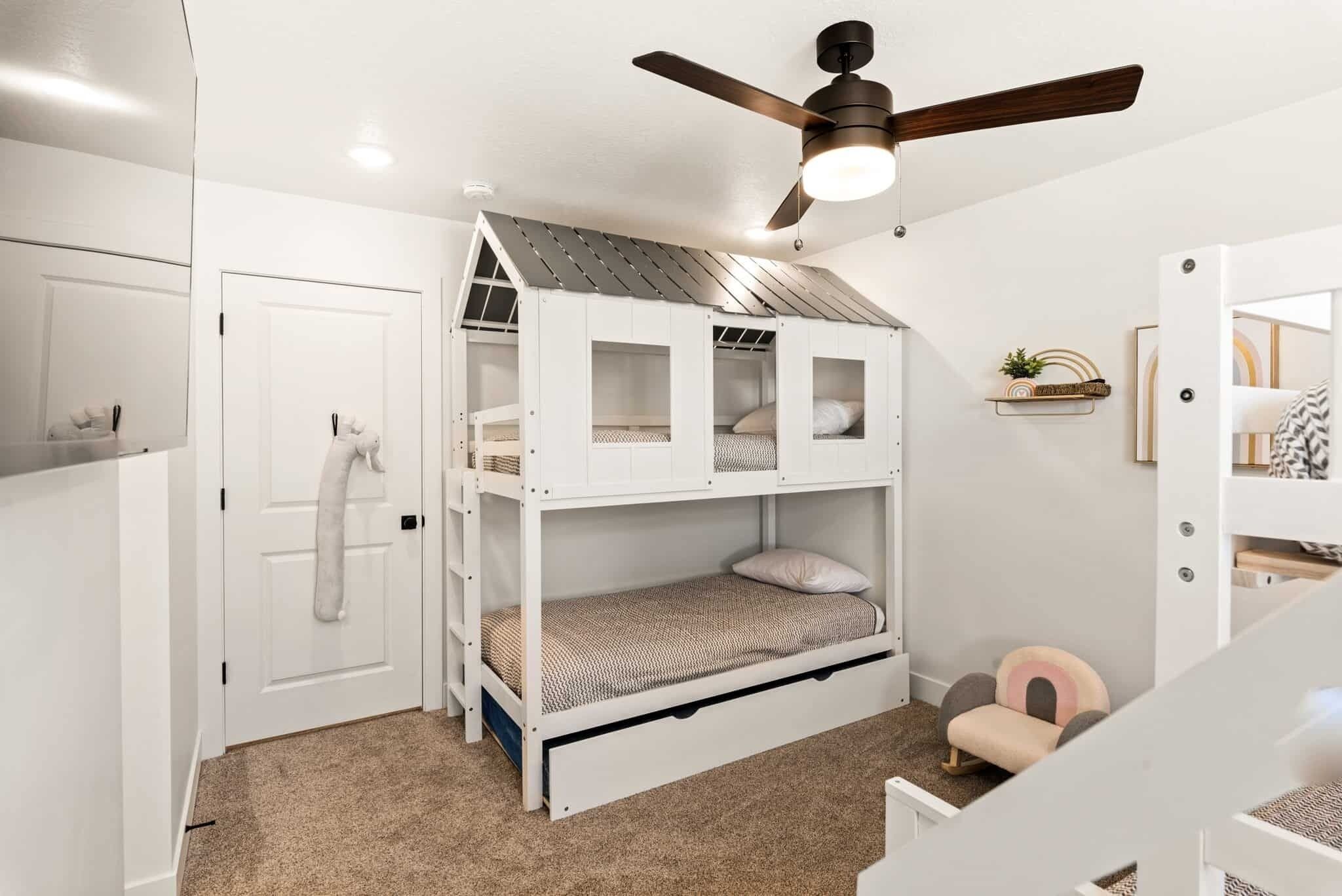 Un lit superposé avec un ventilateur de plafond, une porte blanche et une petite chaise.