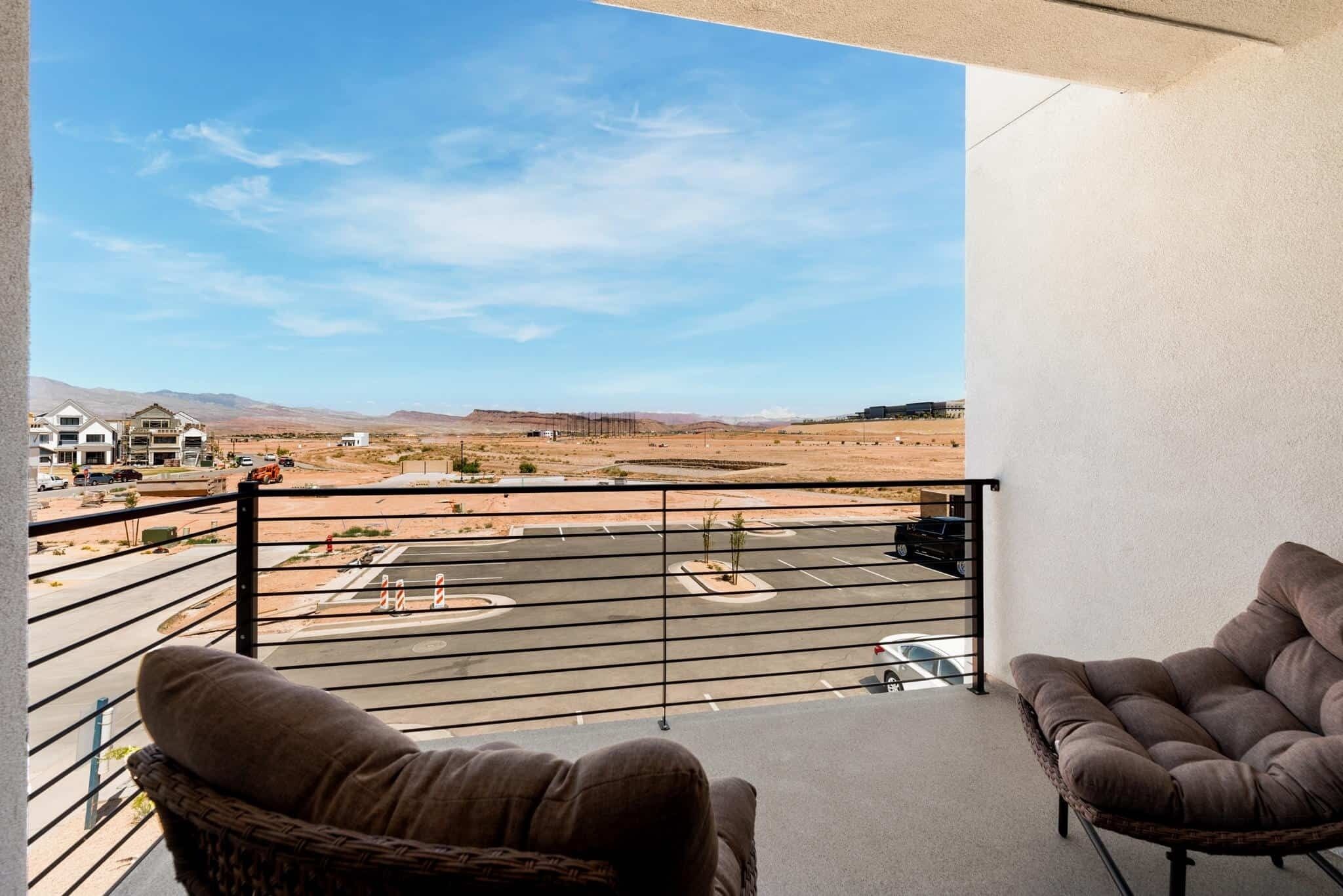 A balcony with two brown cushioned chairs, a view of a parking lot, and distant mountains.