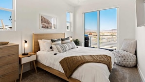 A bedroom with a large bed, a nightstand, a wooden dresser, a ceiling fan, and a view of a balcony with a railing. - Chillin Out Maxin #96 by RedAwning (St. George)