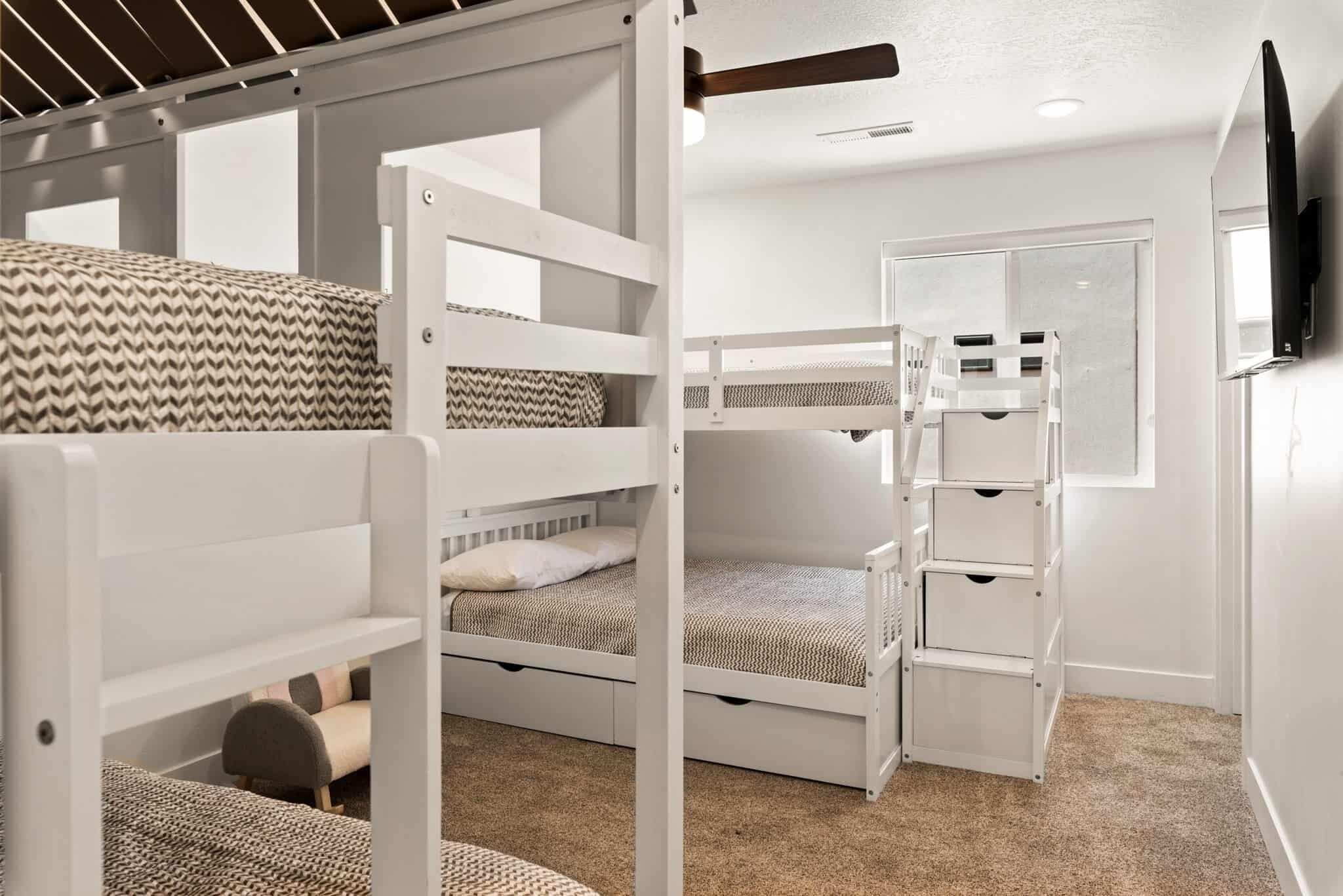 Une chambre avec un lit superposé aux montants blancs, un ventilateur de plafond et une porte avec un miroir.