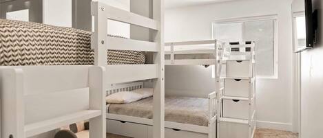 Une chambre avec un lit superposé aux montants blancs, un ventilateur de plafond et une porte avec un miroir.
