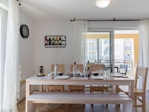 A dining area with a wooden table set for four, a wine rack on the wall, and a view of a balcony with white railings.