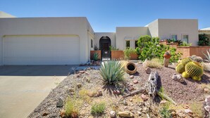 Une maison moderne avec un garage blanc, une porte d’entrée et un petit jardin agrémenté de cactus et de plantes succulentes.