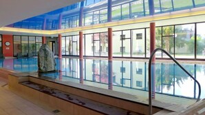 A modern indoor swimming pool with clear glass walls, a stone sculpture, and a staircase leading to the pool. - Enzian 720 by Interhome (Beatenberg)