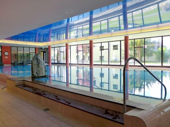 Une piscine intérieure moderne avec des parois en verre transparent, une sculpture en pierre et un escalier menant à la piscine.