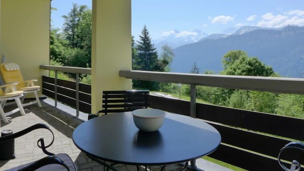 Een balkon met een tafel, stoelen, een schaal en uitzicht op een berg.