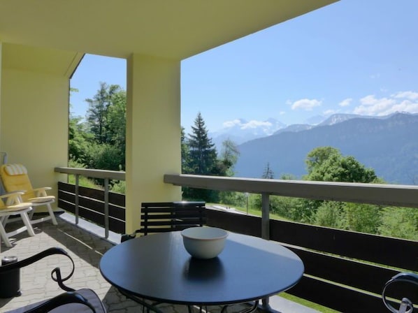 Un balcón con mesa y sillas, un cuenco, y vistas a la montaña.