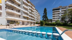 Una piscina con solárium de baldosas, rodeada por un edificio de varios pisos con balcones.