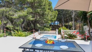 Un área de comedor al aire libre con una mesa de vidrio, sillas de metal y vista a la piscina.