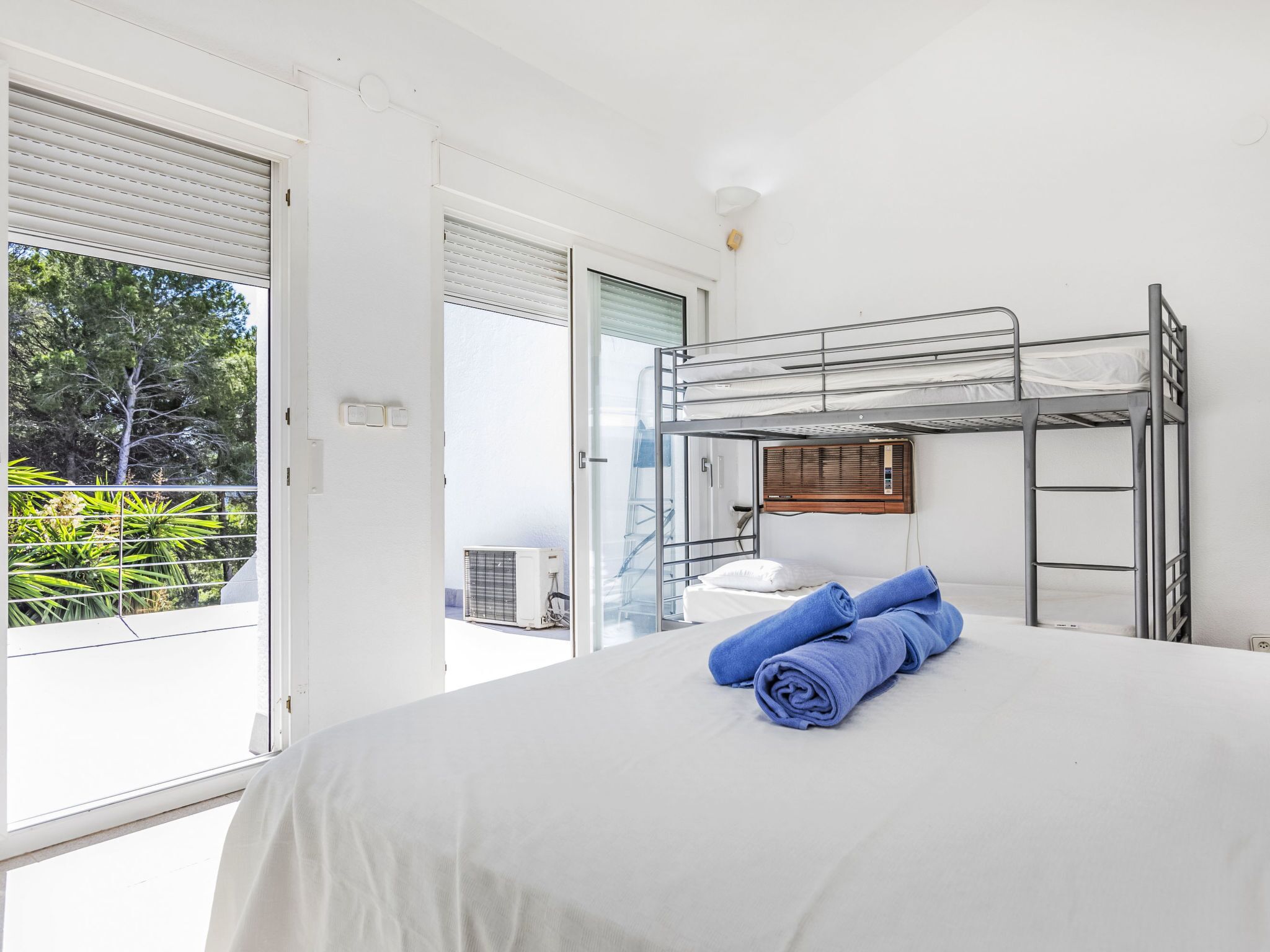 Habitación con literas, una colcha blanca, un par de toallas enrolladas y una ventana con persianas.