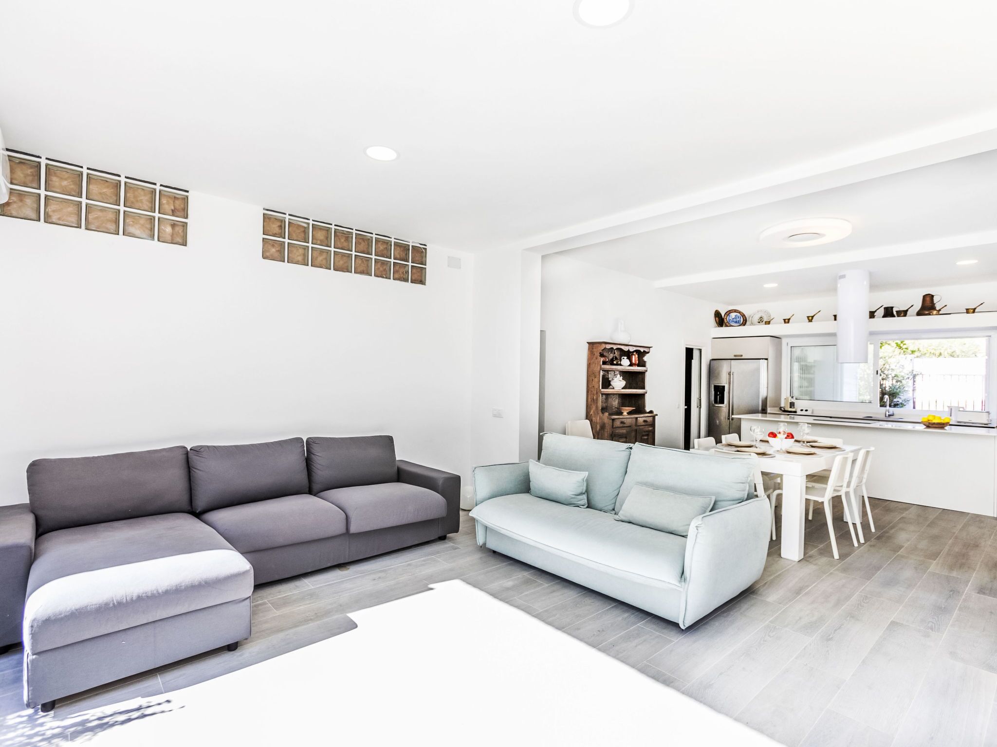 Un salon moderne avec un canapé gris, un canapé bleu clair et un coin repas comprenant une table et des chaises blanches.